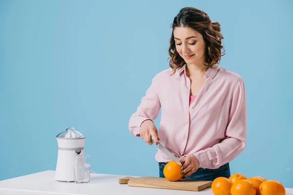 Pretty woman cutting orange on wooden cutting board isolated on blue — Stock Photo