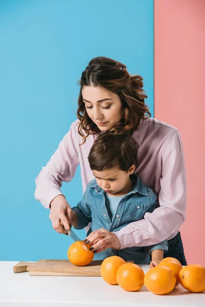 Mother with cute little son cutting oranges together on bicolor background — Stock Photo