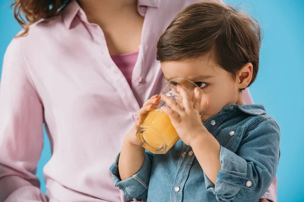 Entzückender kleiner Junge trinkt frischen Orangensaft isoliert auf blau — Stockfoto