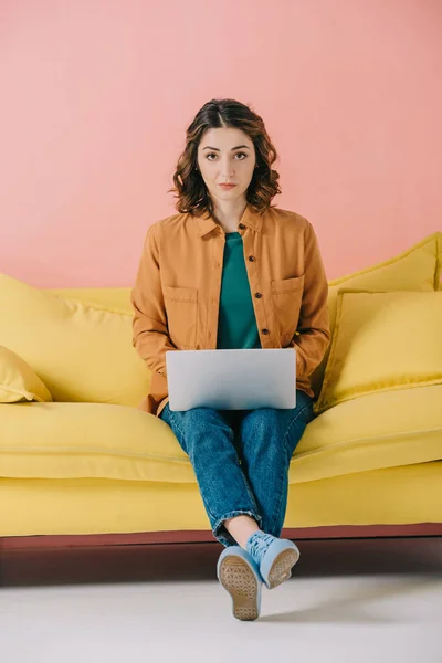 Bela jovem mulher sentada no sofá amarelo e usando laptop — Fotografia de Stock