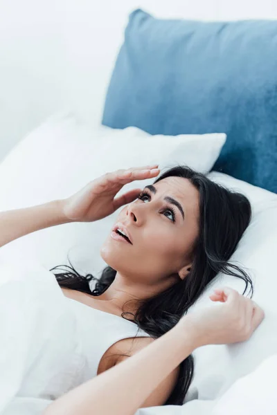 Mujer morena sorprendida acostada en la cama y mirando hacia arriba - foto de stock