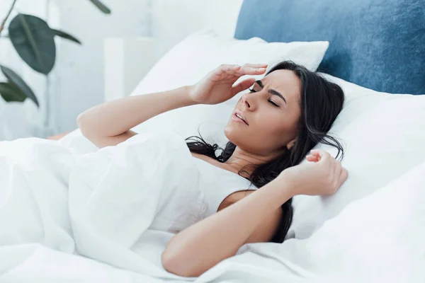 Gereizte brünette Frau liegt mit geschlossenen Augen im Bett — Stockfoto