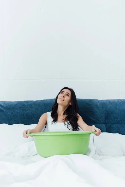 Verärgerte brünette Frau sitzt auf Bett und hält Waschbecken — Stockfoto
