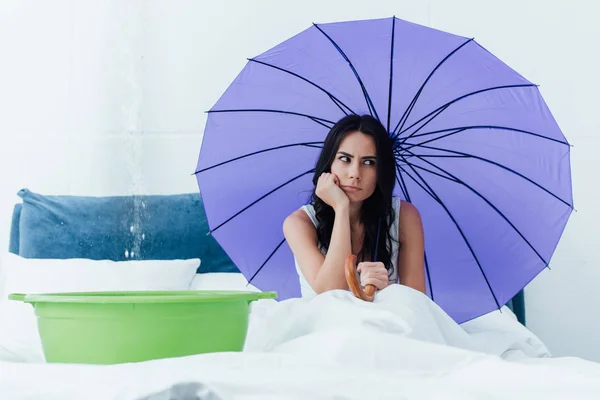 Traurige Frau sitzt bei Wasserschaden mit Regenschirm im Bett — Stockfoto