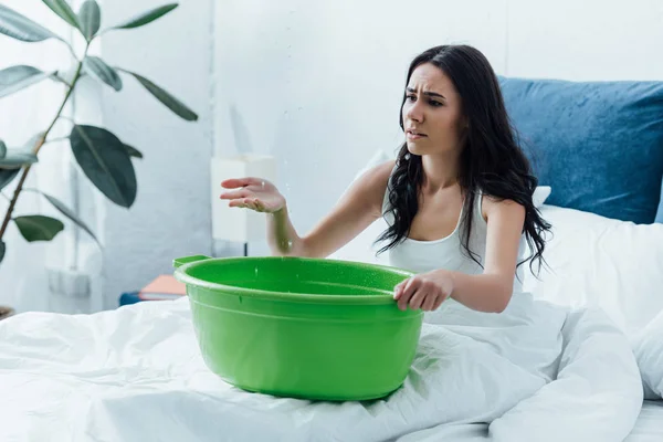 Irritated girl with basin looking at water drops in bedroom — Stock Photo