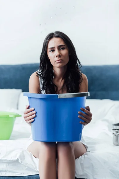 Сумна брюнетка жінка тримає блакитне відро в спальні — стокове фото