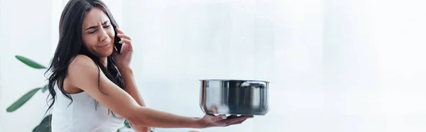 Upset woman talking on smartphone and holding steel pot — Stock Photo