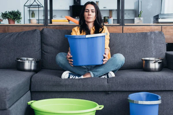 Femme fatiguée assise sur un canapé avec un grand seau bleu — Photo de stock