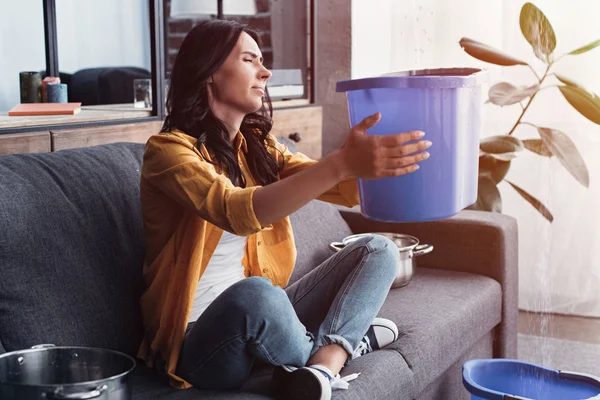 Irritated woman sitting on sofa with blue bucket — Stock Photo