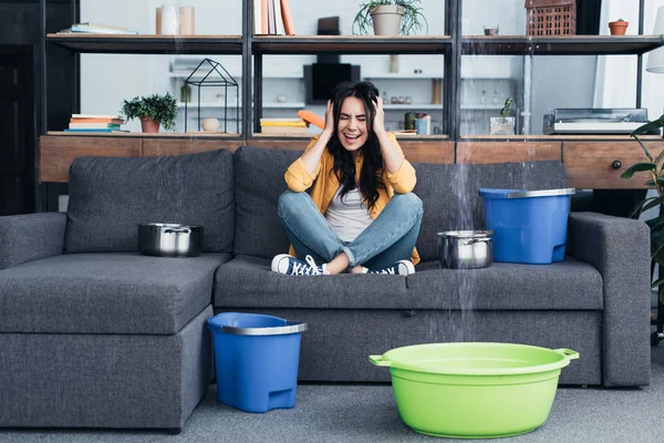 Stressed woman screaming with closed eyes during water leak in living room — Stock Photo