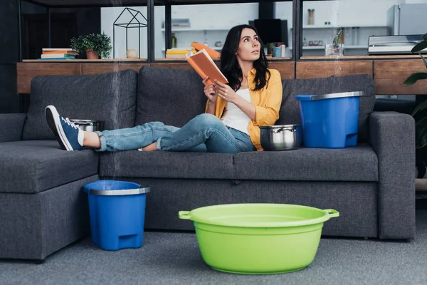 Donna che legge il libro sul divano durante la perdita d'acqua in soggiorno — Foto stock