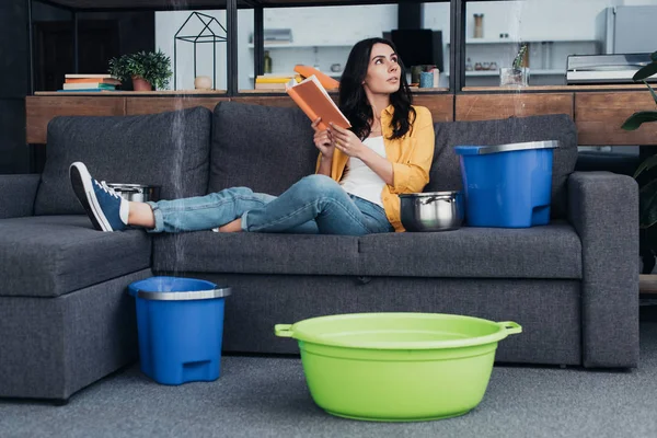 Frau liest Buch auf Sofa bei Wasserleck im Wohnzimmer — Stockfoto