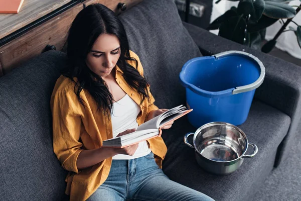 Mulher concentrada em livro de leitura camisa amarela durante vazamento de água na sala de estar — Fotografia de Stock