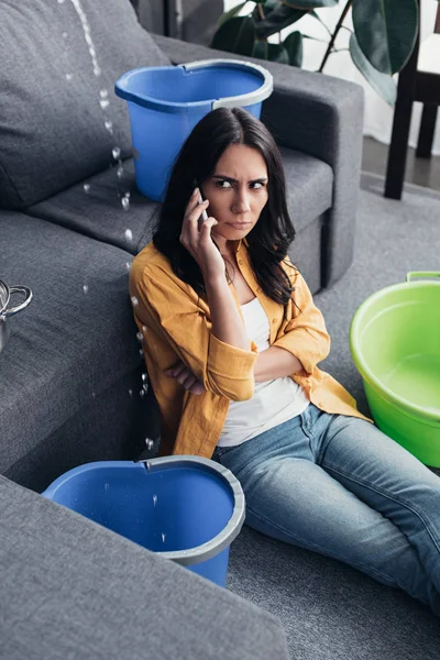 Uspet mulher com smartphone olhando gotas de água na sala de estar — Fotografia de Stock