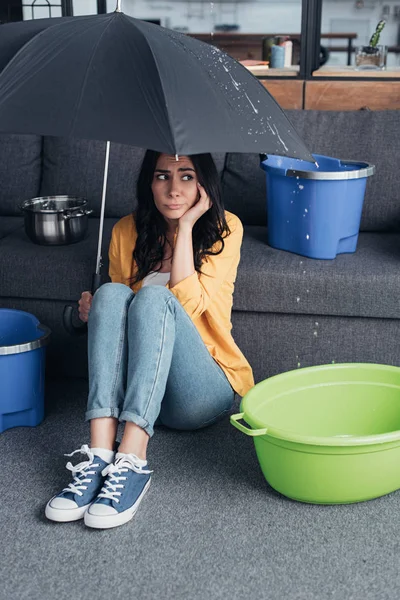 Грустная девушка в джинсах сидит на полу с зонтиком — стоковое фото