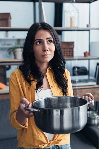 Sad girl in yellow shirt holding pot under water leaking from ceiling — Stock Photo