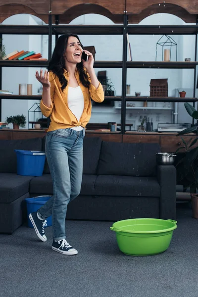 Stressed girl in yellow shirt talking on phone and looking at leaking ceiling — Stock Photo