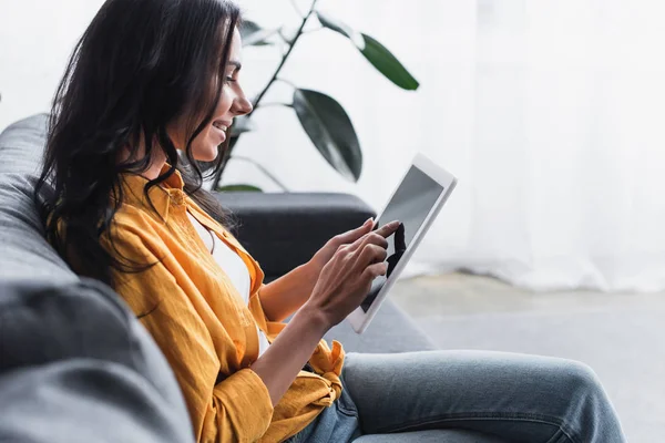 Donna sorridente in camicia gialla seduta sul divano e con tablet digitale — Foto stock