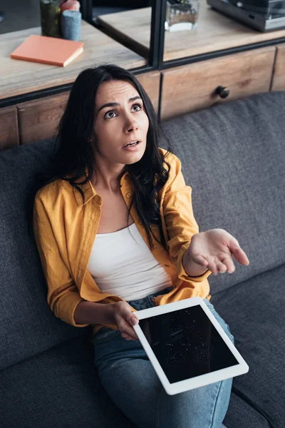 Überraschte Frau sitzt mit wasserbeschädigtem digitalen Tablet auf Sofa — Stockfoto