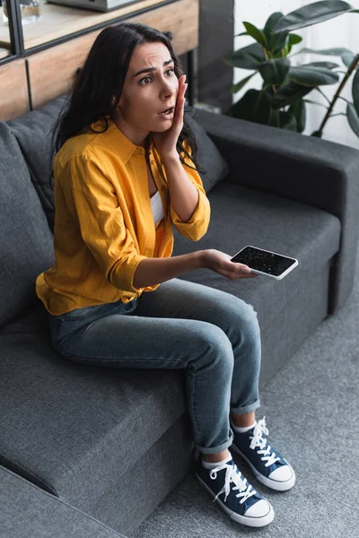 Geschockte Frau mit wasserbeschädigtem Smartphone auf Sofa — Stockfoto