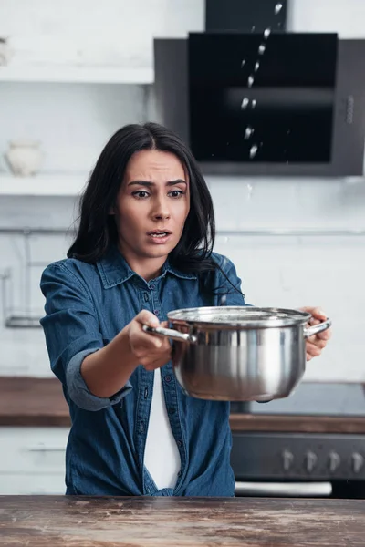 Inquiète jolie femme avec pot traitant de la fuite d'eau dans la cuisine — Photo de stock