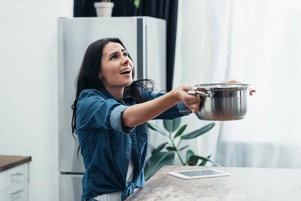 Mujer preocupada en denim corto con olla hacer frente a daños en el agua en la cocina - foto de stock