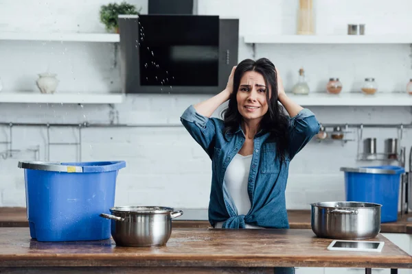 Worried woman touching head during water damage in kitchen — Stock Photo