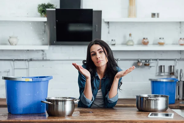 Brunette femme utilisant des pots et des seaux pendant la fuite dans la cuisine — Photo de stock