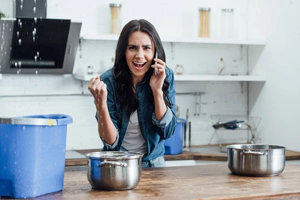 Femme irritée appelant plombier tandis que l'eau fuit dans le seau du plafond — Photo de stock