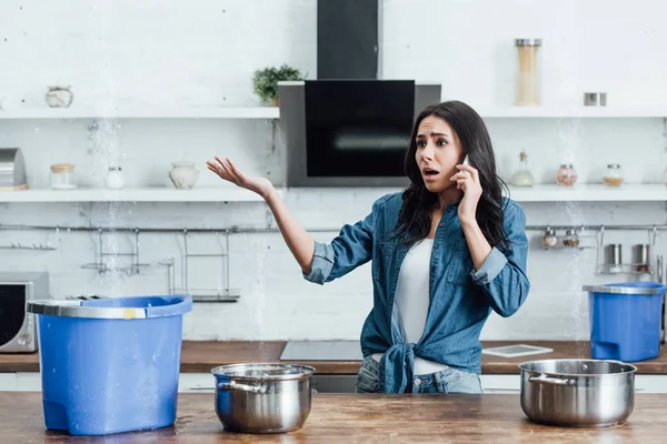 Worried woman looking at water leaking from ceiling and calling plumber — Stock Photo