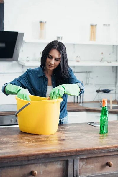 Pleased woman in rubber gloves using plastic bucket in kitchen — Stock Photo