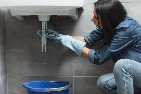 Mujer morena en guantes de goma reparación de tuberías - foto de stock