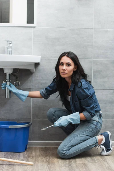 Серьёзная женщина в джинсах чинит трубу в ванной — стоковое фото