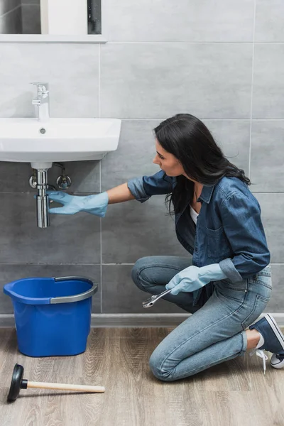 Brunette girl in jeans repairing pipe with wrench — Stock Photo