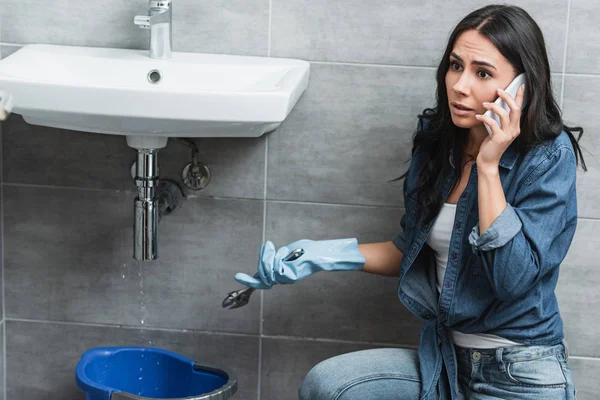 Besorgte Frau spricht mit Smartphone und hält Schraubenschlüssel in der Hand — Stockfoto