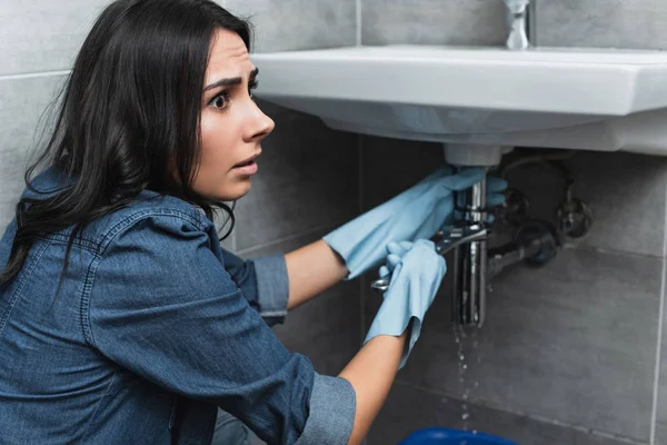 Inquiète fille brune en denim chemise réparer tuyau d'évier avec clé — Photo de stock