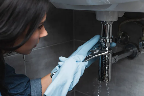 Chica morena en guantes de goma tubo de fijación con llave inglesa - foto de stock