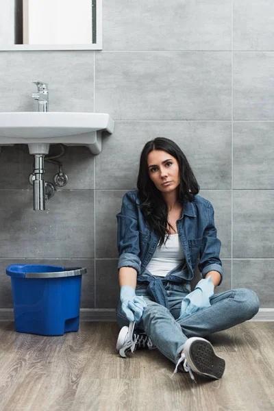 Müde Frau mit Schraubenschlüssel sitzt auf dem Boden im Badezimmer — Stockfoto