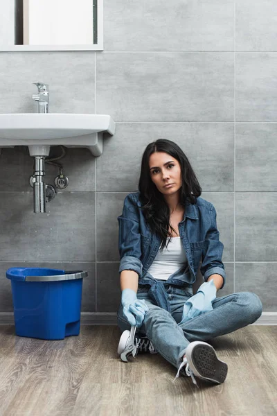 Mulher cansada com chave sentada no chão no banheiro — Fotografia de Stock