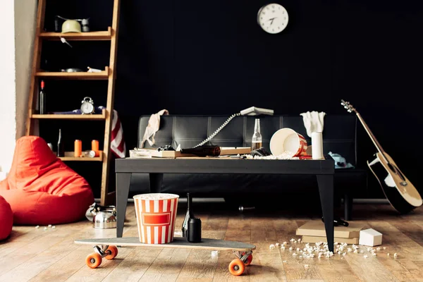 Skateboard with food and drinks in messy living room — Stock Photo