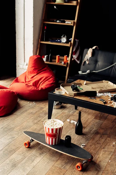 Skateboard with popcorn box near coffee table in messy living room — Stock Photo