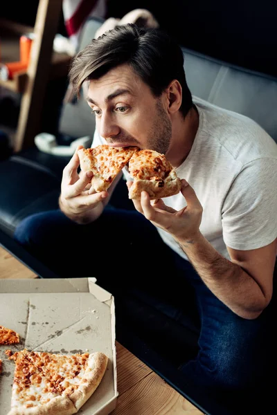 Hungry man eating tasty pizza in living room — Stock Photo