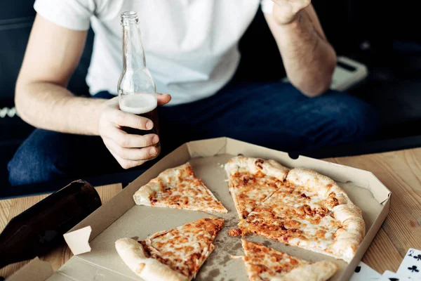 Обрезанный вид человека, держащего бутылку рядом с вкусной пиццей — стоковое фото
