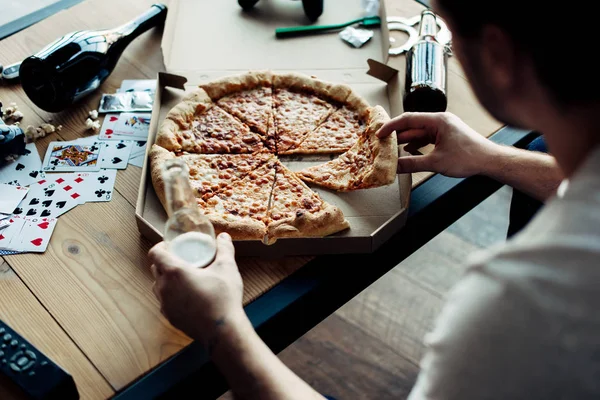 Vista cortada do homem tomando fatia de pizza na sala de estar bagunçada — Fotografia de Stock