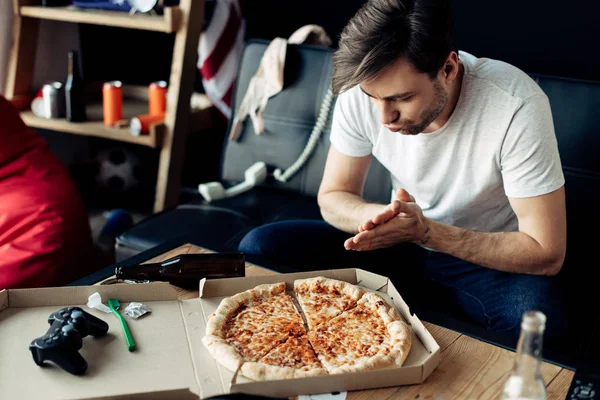 Man looking at tasty pizza in messy living room after party — Stock Photo