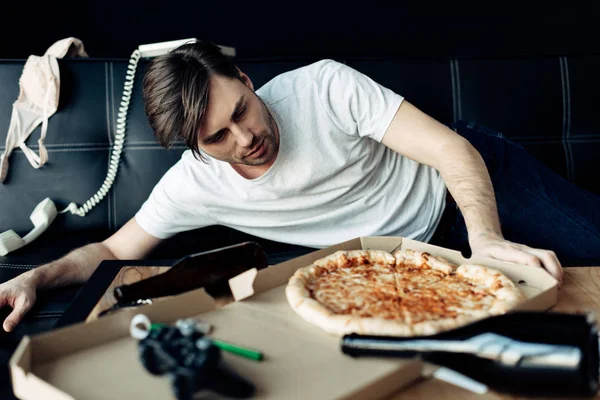 Drunk man looking at tasty pizza at messy home after party — Stock Photo