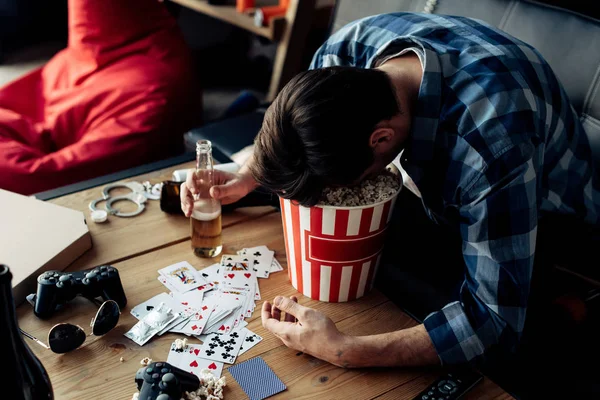 Hombre durmiendo con la cabeza en palomitas de maíz botella de celebración en casa - foto de stock