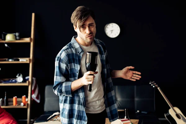 Drunk man holding bottle in messy living room — Stock Photo