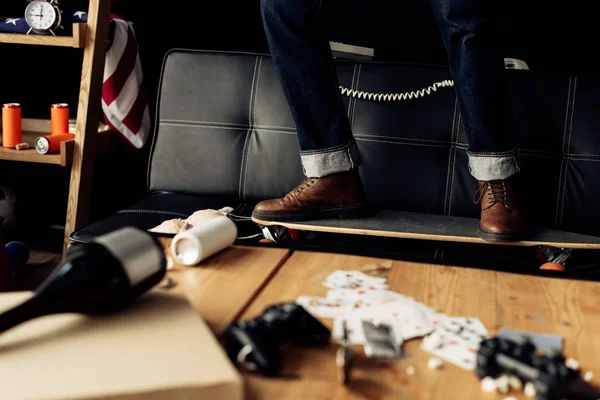 Vista recortada del hombre de pie en el monopatín cerca de la mesa de centro con botellas - foto de stock