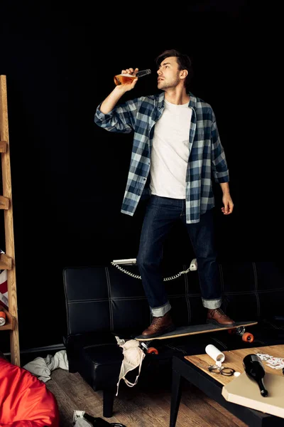 Hombre de pie en el monopatín y beber cerveza de la botella después de la fiesta en casa - foto de stock